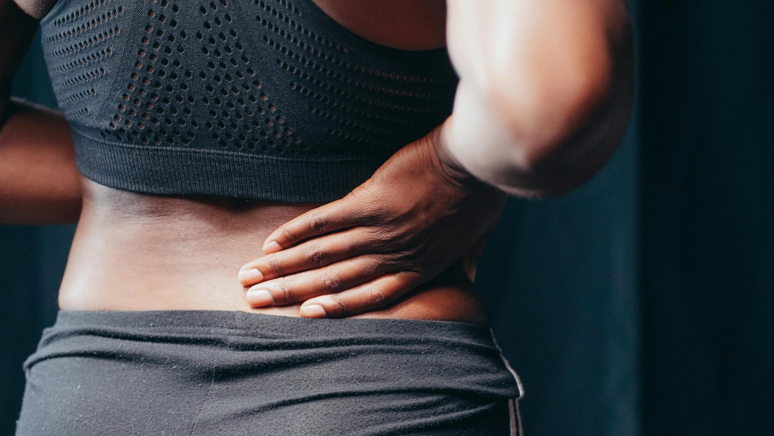 An adult of African descent holding their lower back in pain, indicating discomfort or injury.